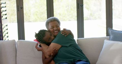 African grandmother hugging granddaughter on sunlit sofa warm family embrace and joy