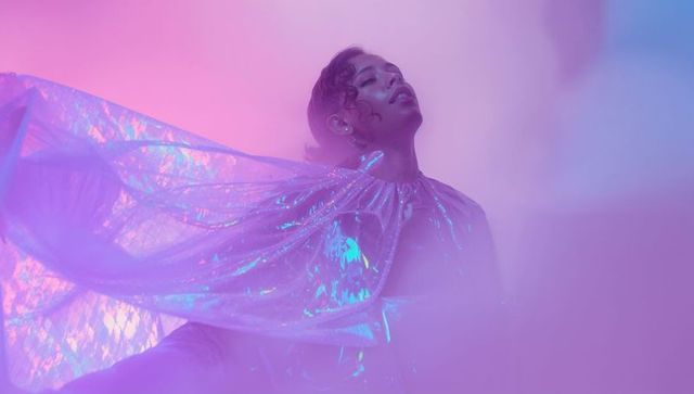 Futuristic Female Model in Holographic Cape Among Pink and Purple Haze