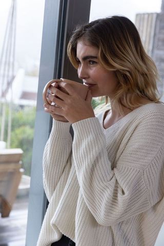 Serene Woman in Knit Sweater Enjoying Coffee by Window