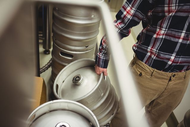 Midsection of manufacturer holding kegs in brewery