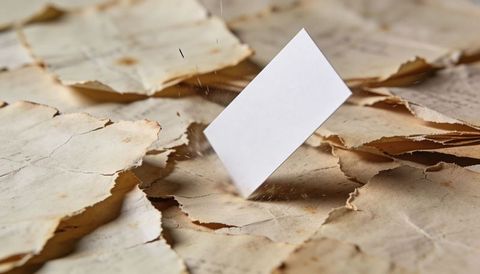 Blank white card landing on torn vintage paper layers, fibers scattering, dramatic shadow
