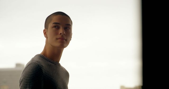 Young man in urban setting gazing out window. Perfect for promoting reflective and introspective themes, mental health awareness, urban lifestyle blogs, and fashion. 