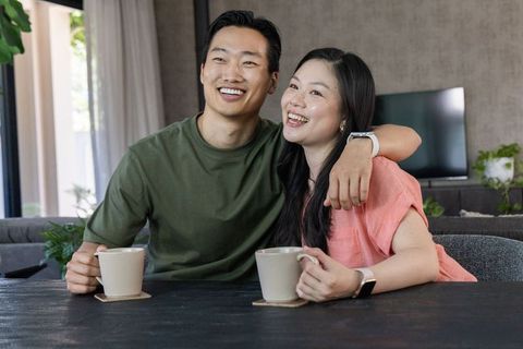 Smiling diverse couple sharing coffee and cuddles in modern living room, cozy lifestyle