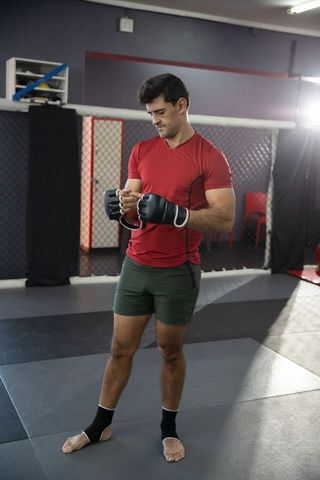Mma fighter adjusting hand wraps and gloves before sparring on padded mat in cage