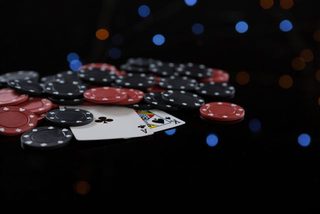 This image shows a close-up view of poker chips and playing cards on a black background with bokeh lights in the background. It is ideal for use in articles or advertisements related to casinos, gambling, nightlife, and entertainment. It can also be used for illustrating concepts of risk, strategy, and leisure activities.