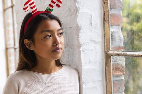 Woman with candy cane headband gazes out rainy window