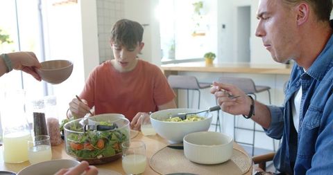Modern family sharing healthy dinner with salad and pasta in bright kitchen