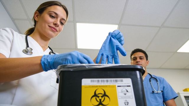 Female clinician disposing blue gloves into biohazard container in medical clinic