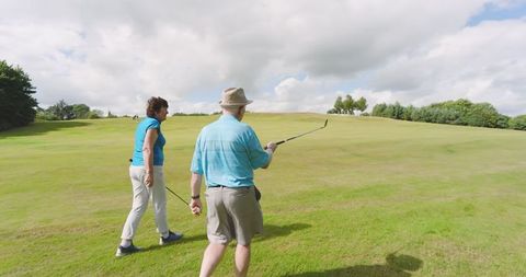 Senior couple enjoying golfing on lush green fairway under cloudy sky