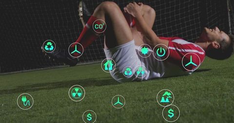 Injured soccer player clutching knee on artificial turf surrounded by green energy icons
