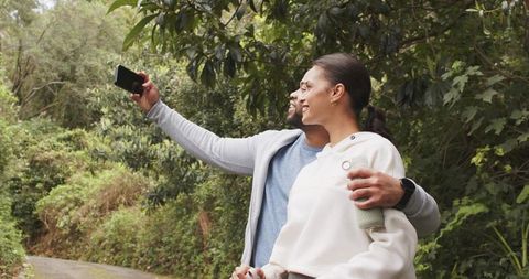 Couple taking selfie on wooded trail during casual hike holding reusable bottle