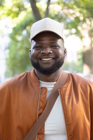Smiling man wearing beige cap and rust-orange bomber jacket portrait outdoors