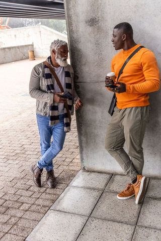 Multigenerational african american men leaning and chatting at urban plaza with coffee