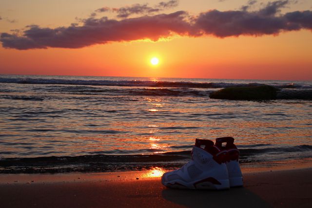 These sneakers are placed on a sandy beach as the sun sets over the ocean, producing a dramatic and colorful sky. Ideal for illustrating themes of adventure, travel, relaxation, nature, and beach vacations. Suitable for use in advertisements for footwear brands, travel agencies, outdoor gear marketing, or blog posts about beach destinations and peaceful moments.