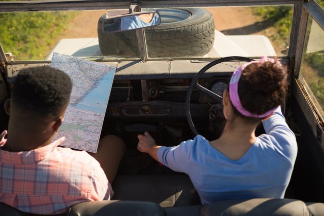 Couple navigating with a map while driving on a countryside road trip. Ideal for travel blogs, adventure planning, vacation advertisements, and articles on road trips and outdoor exploration.