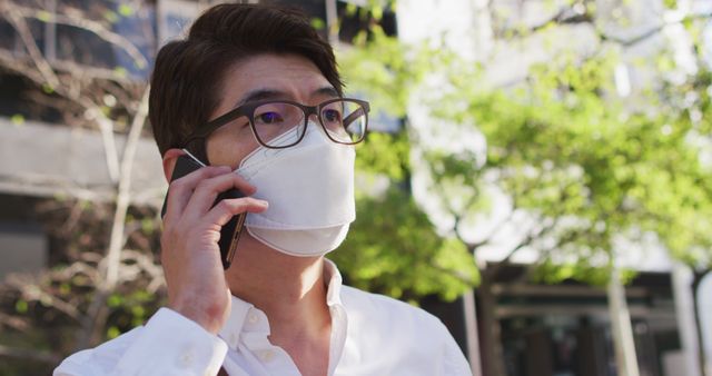 Asian man wearing face mask talking on smartphone on the street. health protection and safety during covid-19 pandemic concept