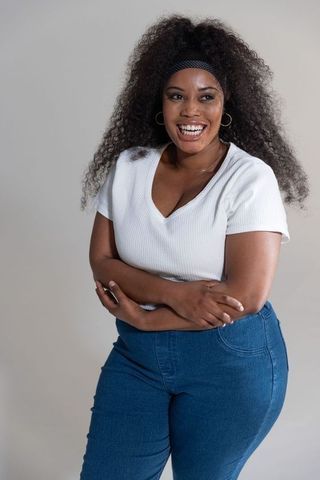 Mid-adult african american woman laughing and posing in casual white top, blue jeans