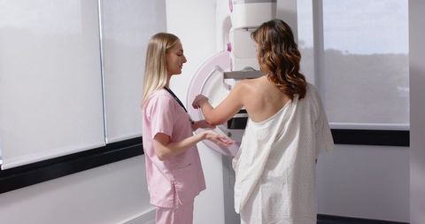 Radiology technician guiding patient during mammogram screening and breast compression