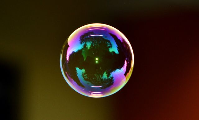 Close-up of a floating soap bubble showcasing vibrant, iridescent colors and reflections on a dark background. Image perfect for concepts involving fragility, beauty, and the ephemeral nature of life. Suitable for design projects, educational materials, and artistic inspiration.