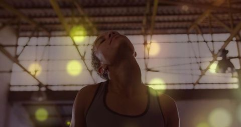 Athlete tilting head back after intense training under industrial skylight with soft bokeh