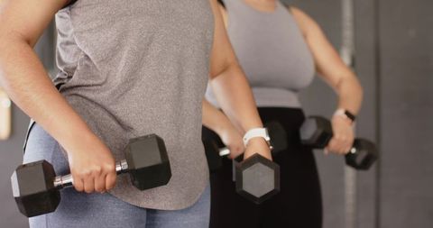 Two women holding hex dumbbells during strength training showing smartwatch on wrist