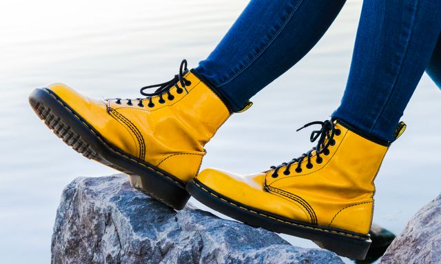 Bright yellow boots paired with denim jeans while perched on rock by water, perfect for highlighting fashion choices, casual outdoor activities, youth culture, or travel-related themes.