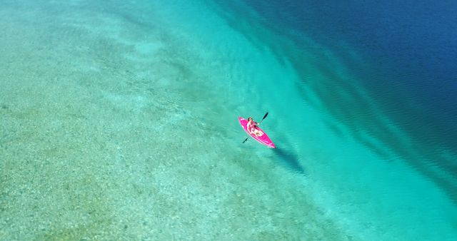 Aerial perspective of a woman kayaking in crystal clear, vibrant blue ocean. Great for travel blogs, outdoor adventure websites, tourism brochures, water sport promotions, and relaxation-themed marketing campaigns.