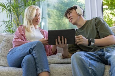 Mother and teen sharing tablet on sofa, relaxed family tech moment at home