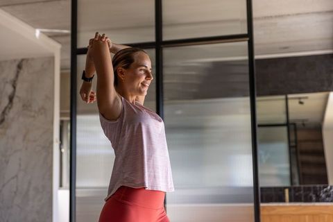 Woman stretching upper body and smiling in modern studio wearing athleisure and smartwatch
