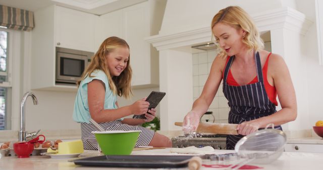 Caucasian mother and daughter using digital tablet and baking together in the kitchen at home. family, love and togetherness concept