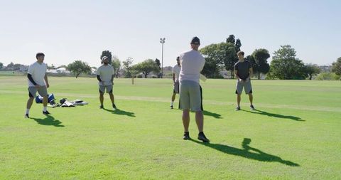 Coach leading diverse male cricket fielding drill on sunny green sports field