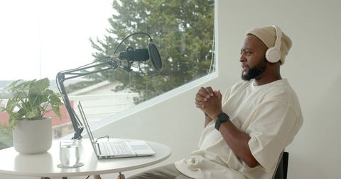 Recording podcast from home workspace with boom microphone, laptop and headphones