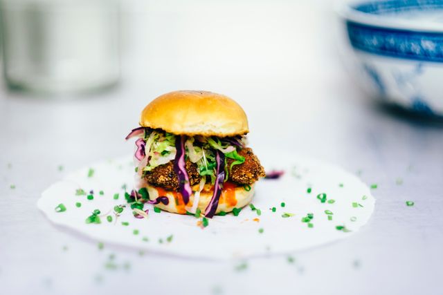 Vegan slider featuring crispy avocado and fresh slaw on a white plate, sprinkled with chopped chives on a contemporary table. Ideal for use in vegan food blogs, healthy eating campaigns, restaurant menus, and cooking magazines.