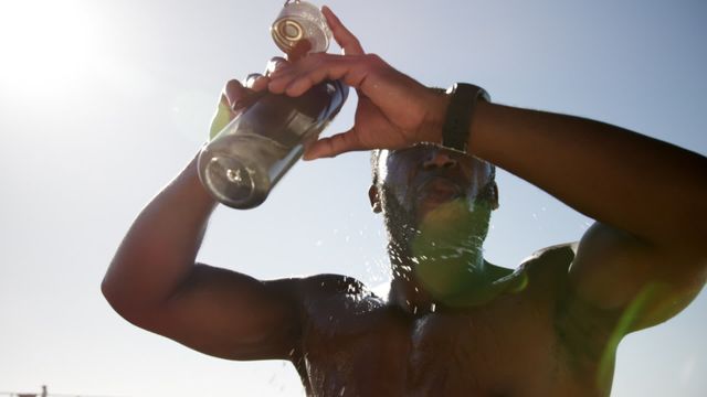 This video shows an African American man cooling himself down by pouring water on his head at the beach. The natural light and the low angle highlight the freshness and the hot summer day. Ideal for use in articles on summer activities, fitness routines, hydration, beach vacations, and lifestyle blogs. Perfect for brands focusing on health, wellness, and outdoor activities.