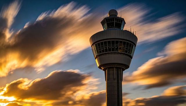 Backlit airport control tower at sunset with long-exposure streaked clouds and radar dome