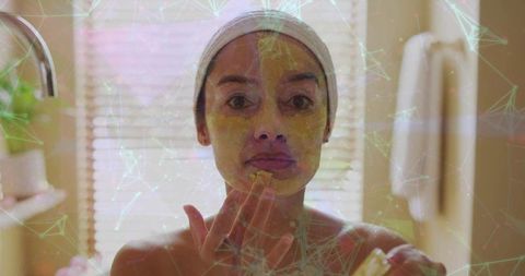 Woman applying yellow facial mask during home spa skincare routine at bathroom vanity