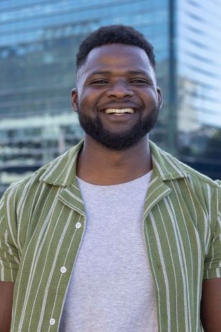 Confident african man smiling in olive green striped shirt at modern glass office plaza