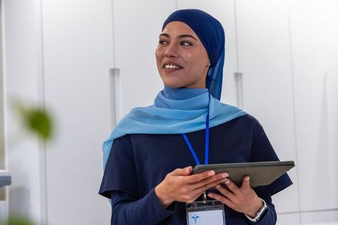 Smiling african healthcare professional wearing two-tone hijab using tablet at reception