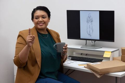 African-american fashion designer pointing at sketch on monitor while holding mug