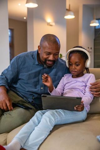 African american father and daughter watching tablet together on cozy modern sofa