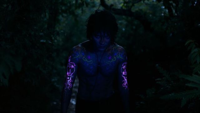 Mysterious man with glowing uv tattoos walking through forest at night