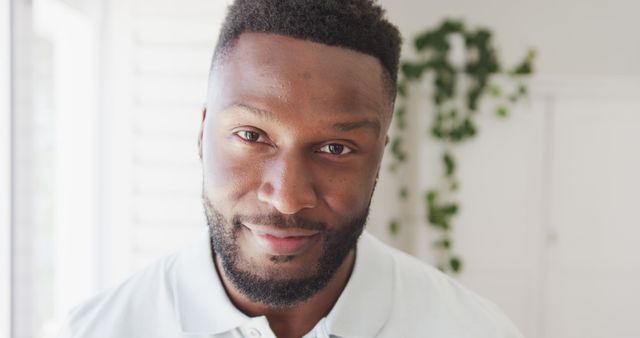 Portrait of young, smiling African American man with a beard in a modern, brightly lit home. This photo could be used for articles on lifestyle, happiness, diversity, or modern living spaces. Suitable for social media, blogs, and marketing materials on related topics.