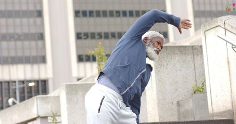 Senior African American man stretching on urban plaza steps in hoodie and sweatpants