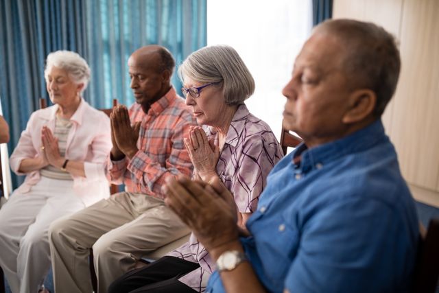Elderly individuals sitting in a row, hands clasped in prayer, creating a serene and spiritual atmosphere. This image can be used for promoting senior living communities, spiritual wellness programs, or articles on aging and faith.