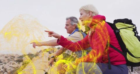 Mature couple hiking and pointing on rocky ridge with backpacks and trekking poles