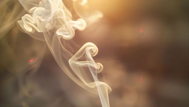 Rising smoke plume forming creamy spirals with amber bokeh and warm sun flare
