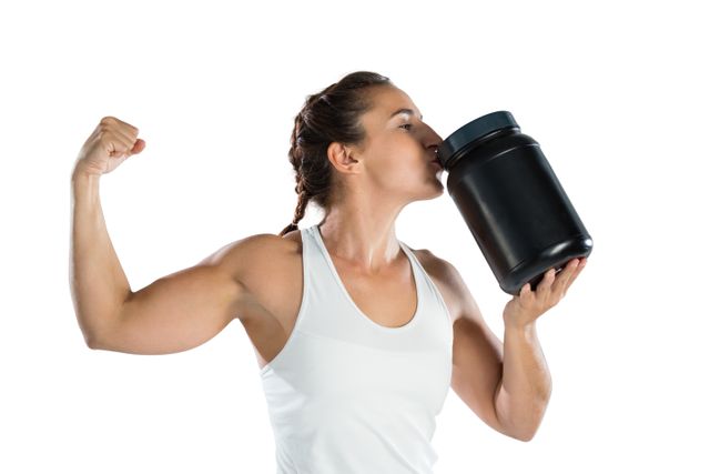 Female athlete flexing muscles while kissing supplement jar while standing against white background
