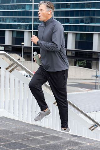 Middle-aged man climbing urban stairs holding water bottle wearing earbuds and smartwatch