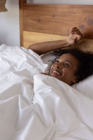African american woman smiling and stretching in cozy white bedding for morning wellness