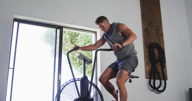 Fit sweaty caucasian man exercising on training bike inside gym. cross training for fitness in gym.